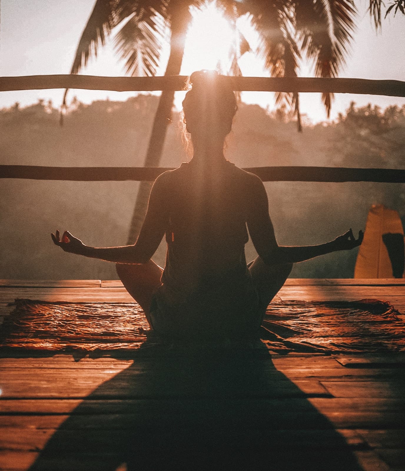 A person meditating cross-legged at sunset under palm trees