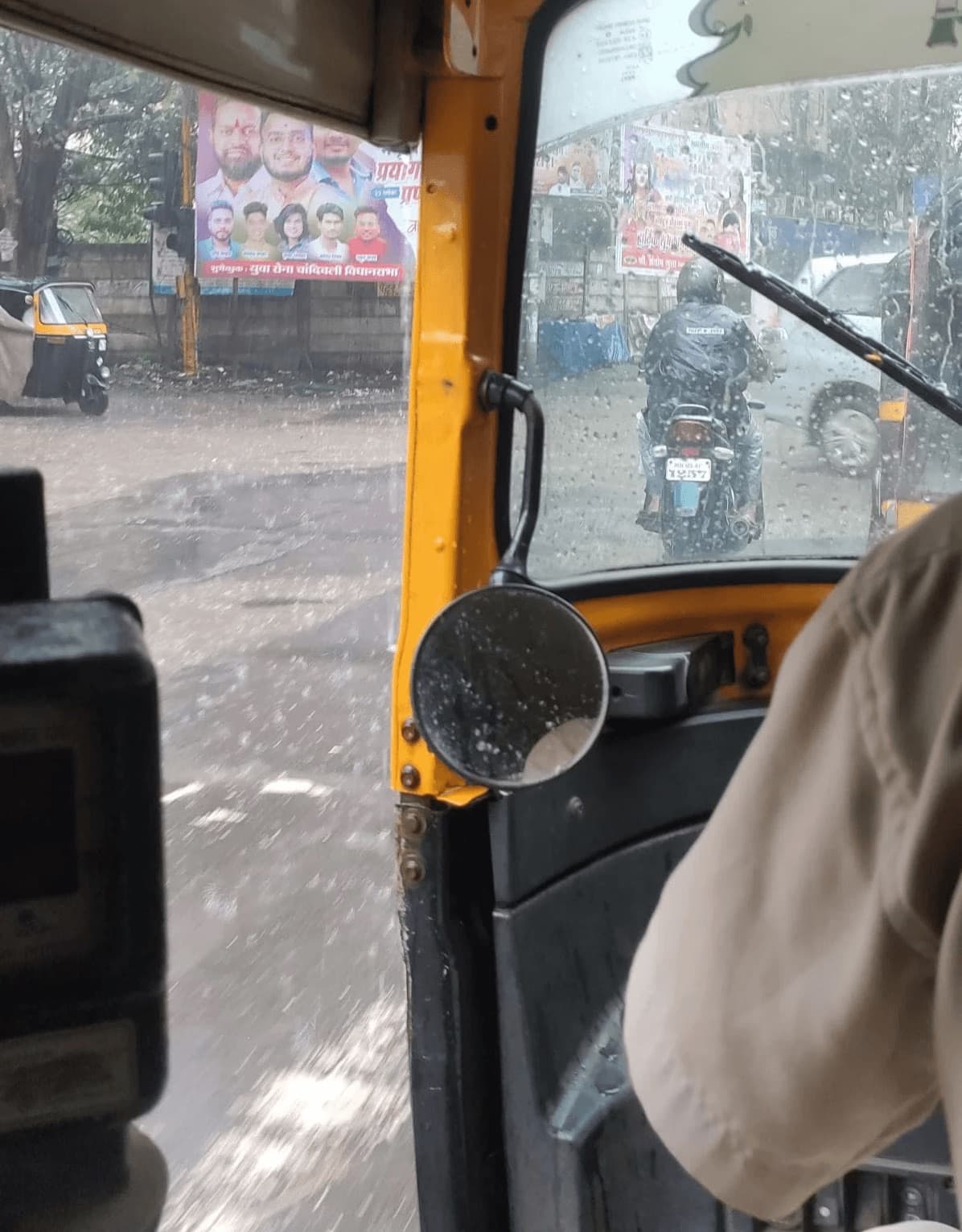 A rainy street seen from the back of an auto rickshaw