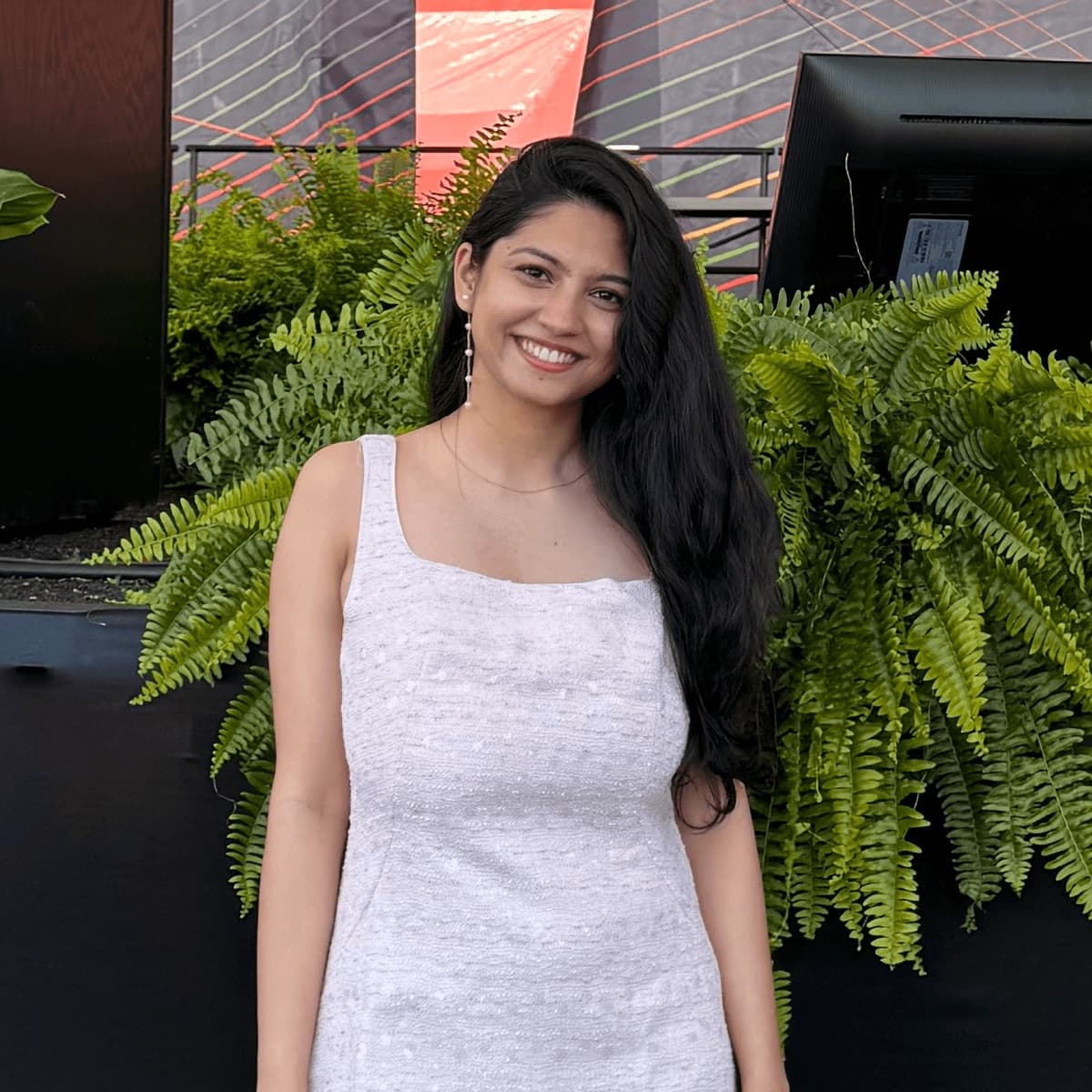 Heena smiling in front of a wall of ferns